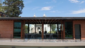 Un edificio moderno con fachada de vidrio, un área de estar al aire libre techada y una vista de un edificio histórico con cúpulas al fondo.