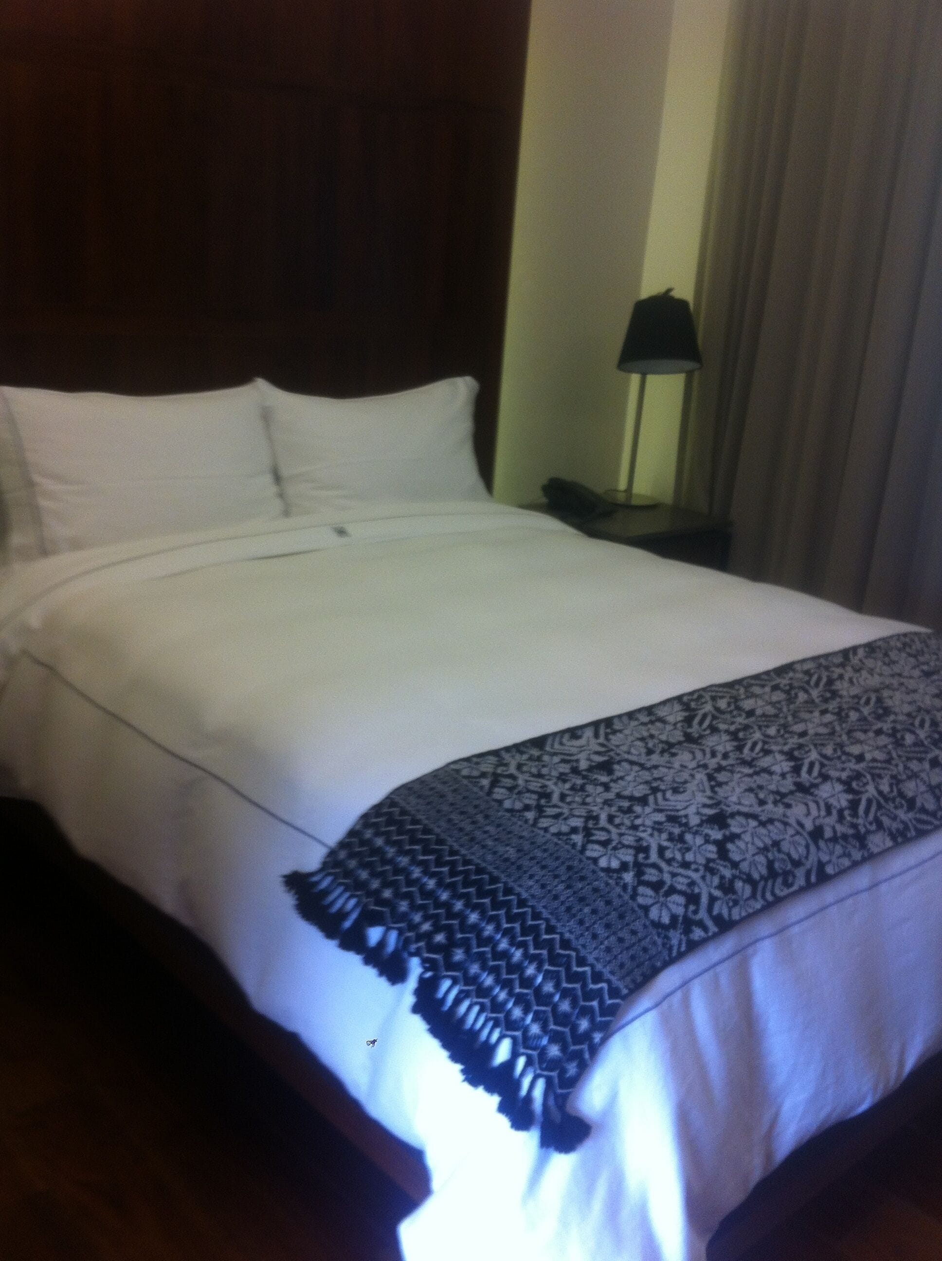 Una cama bien tendida con sábanas blancas y una manta decorativa.