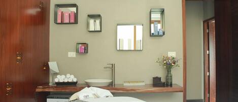 A hotel room with a bed, a wooden wardrobe, a vanity with a sink, and multiple mirrors.