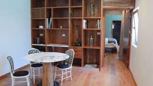 Un comedor con una mesa redonda y cuatro sillas, una estantería de madera con diversos objetos, y vista a otra habitación.