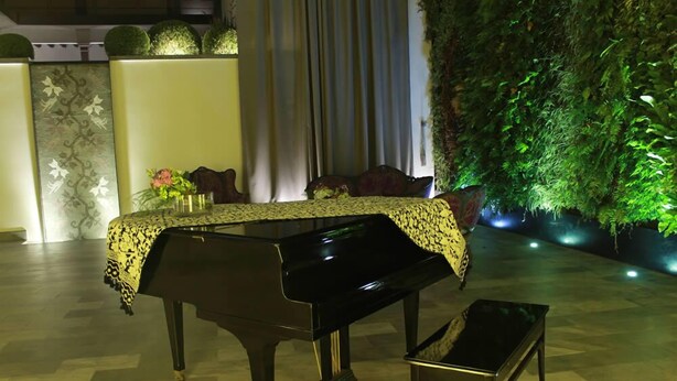 A grand piano with a patterned tablecloth, a bench, and a lush green wall in the background. - Hotel Casa Mixtli (Teziutlan)