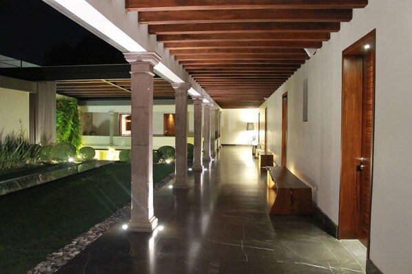 A covered outdoor corridor with a reflective floor, wooden beams, and a door on the right.
