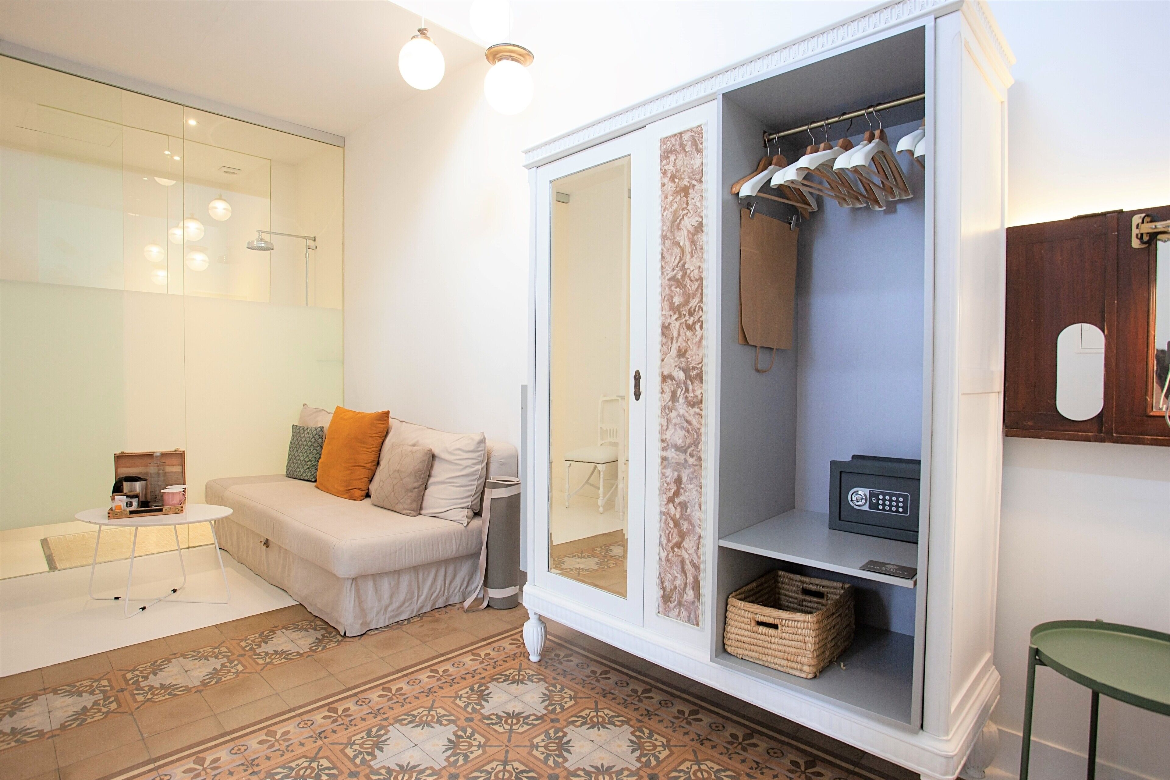 A modern bathroom with a glass shower enclosure, a white vanity with a mirror, and a beige sofa with orange cushions.