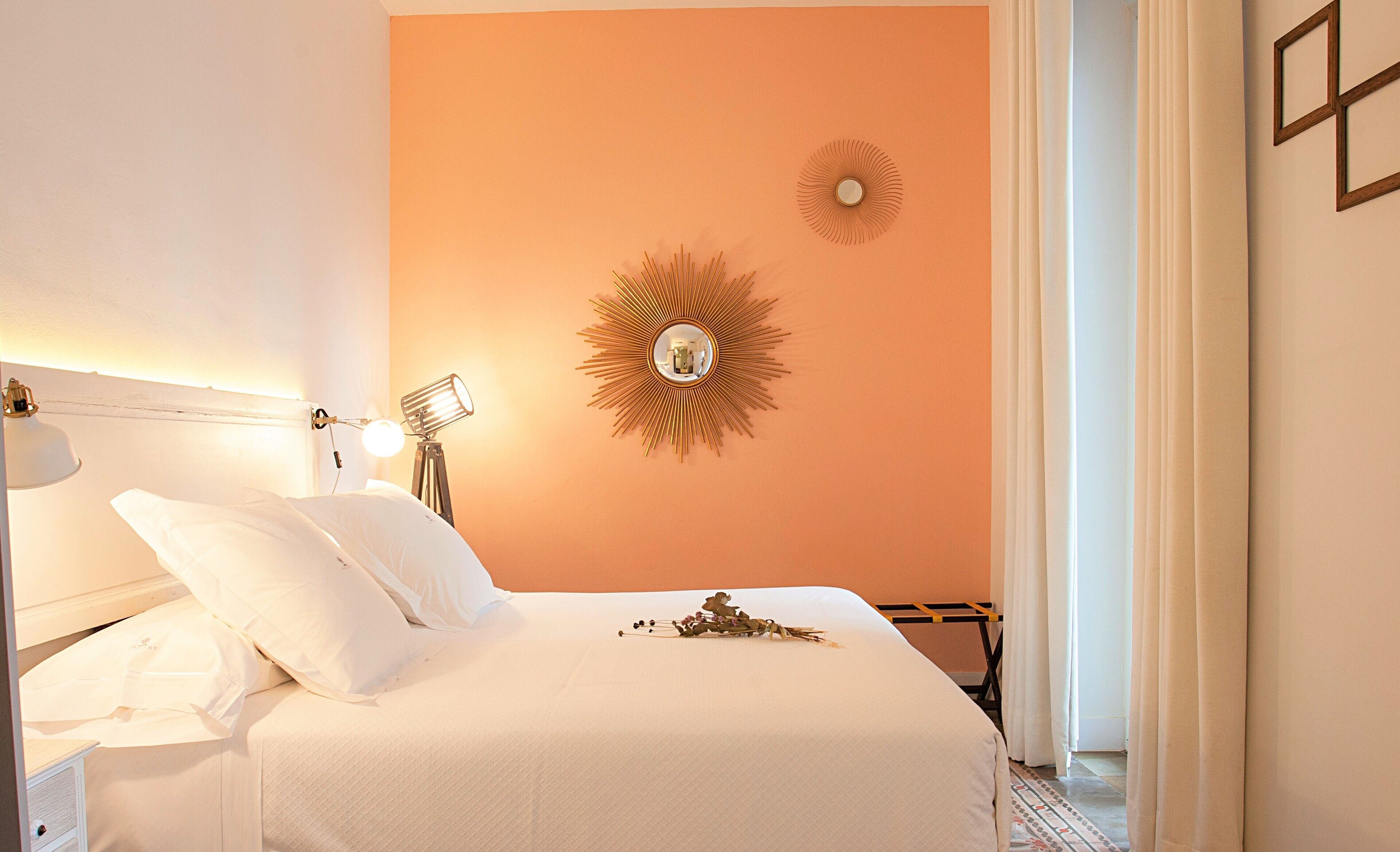 A hotel room with a bed, a nightstand, a lamp, and a wall-mounted mirror.
