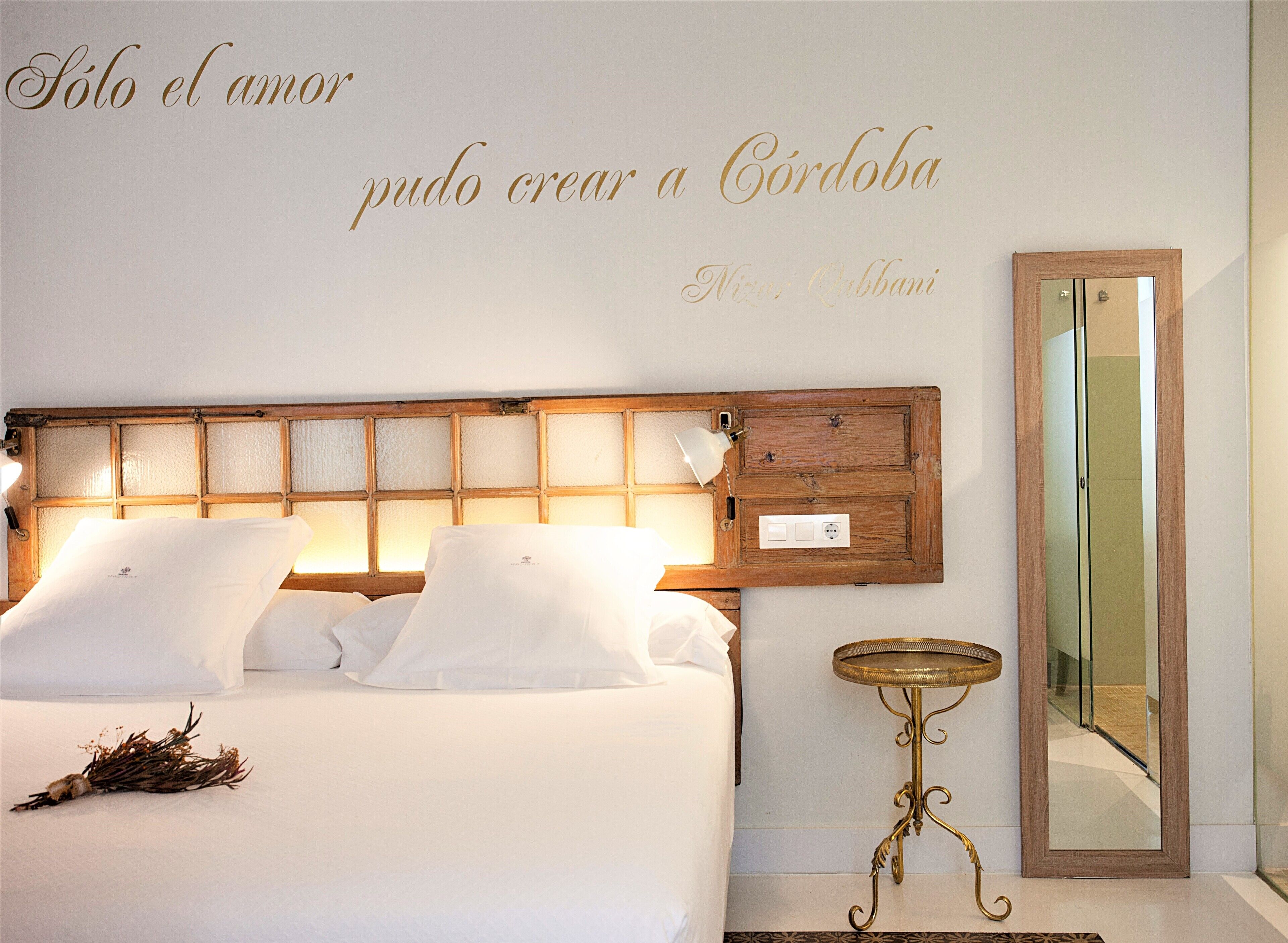 A neatly made bed with white linens and pillows, a bedside lamp, and a small table with a decorative item beside it.