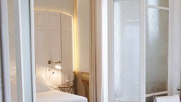 A hotel room with a bed, a small table, and a chair. There is a window with frosted glass and a curtain.