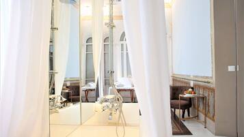 Une salle de bain luxueuse dotée d’un grand miroir, d’une douche moderne et d’un coin salon avec une table et des chaises.