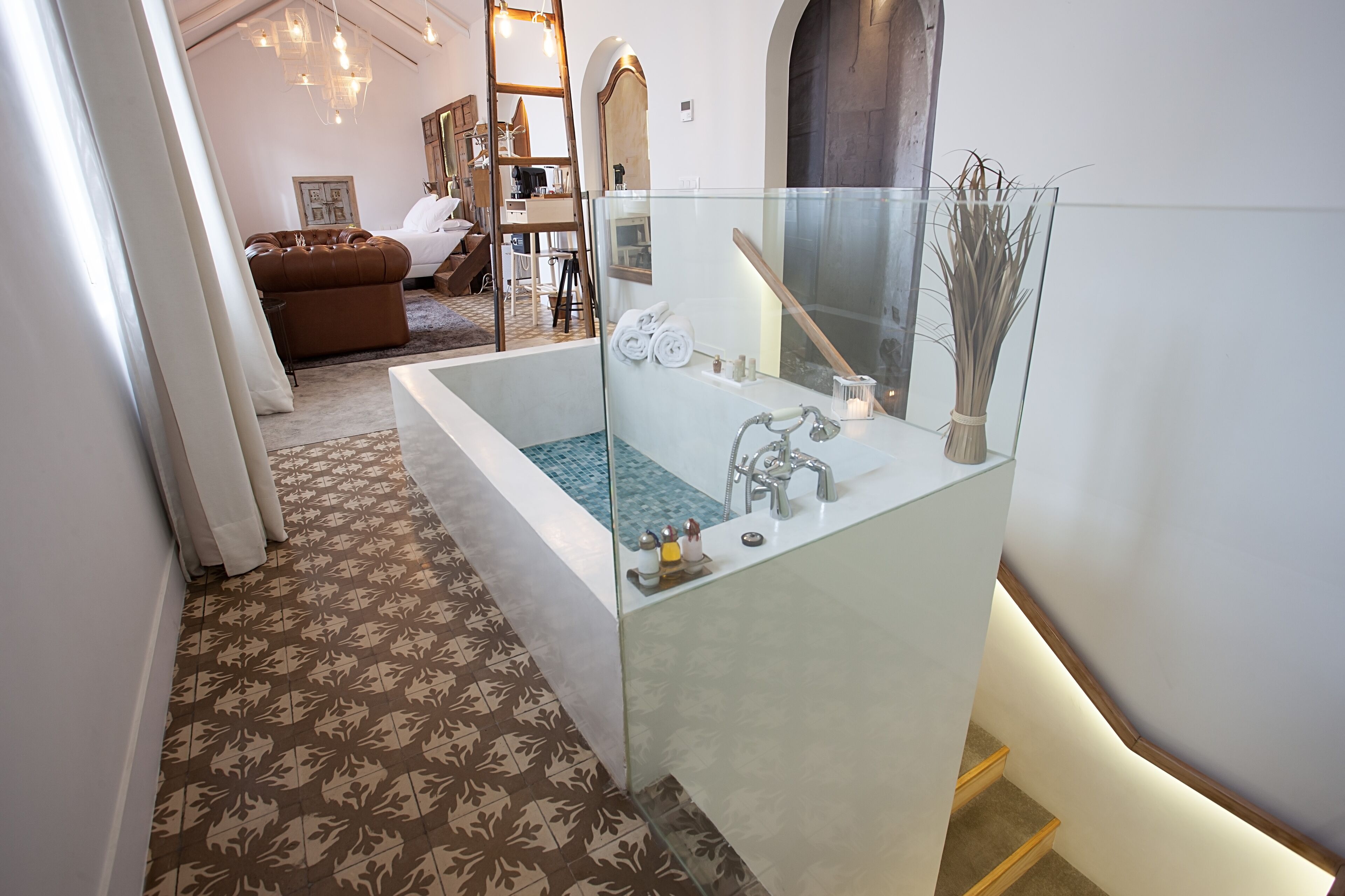 A modern bathroom with a glass-enclosed bathtub, a wooden bench, and a patterned floor.