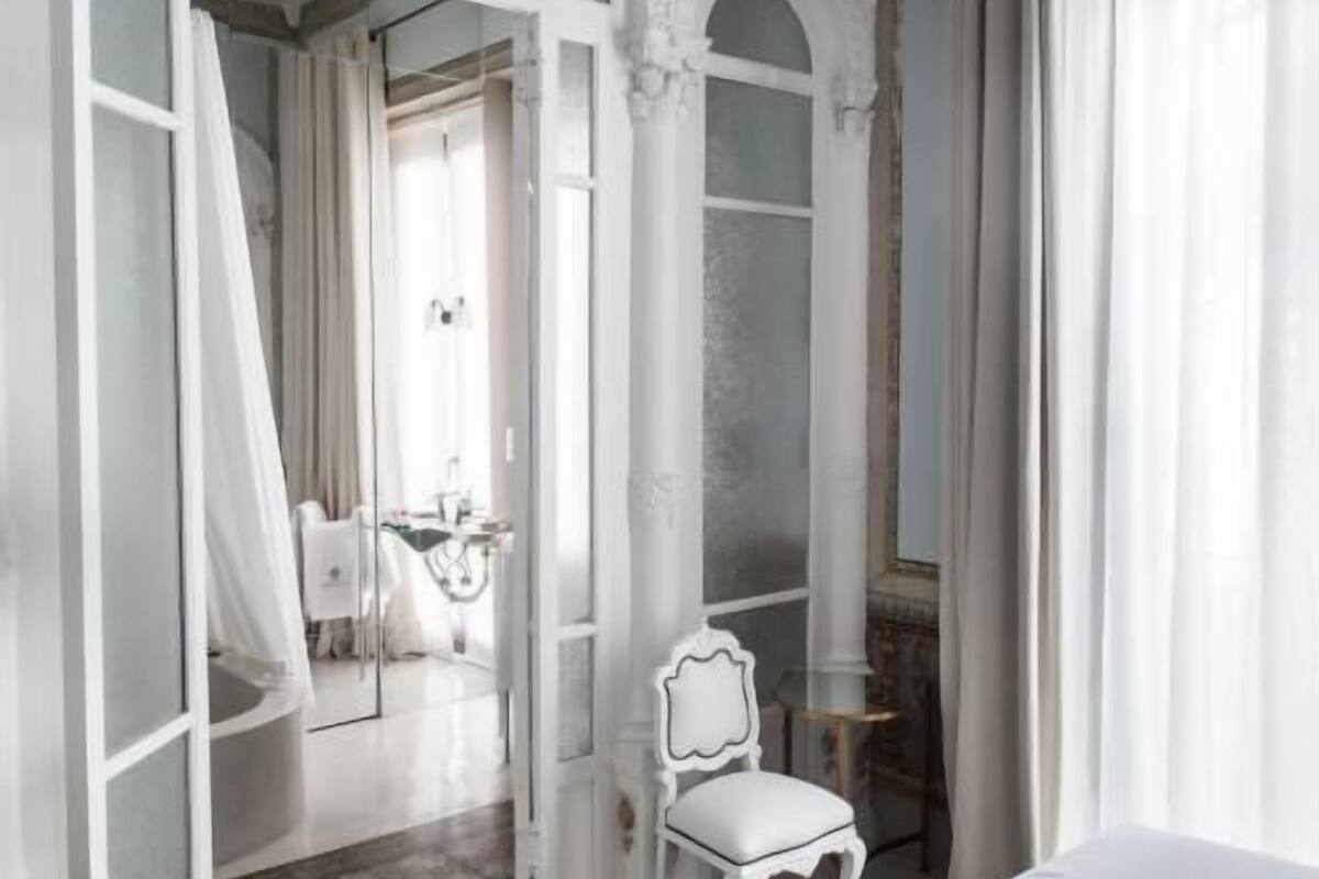 A room with a white chair, a bed, and a mirror.