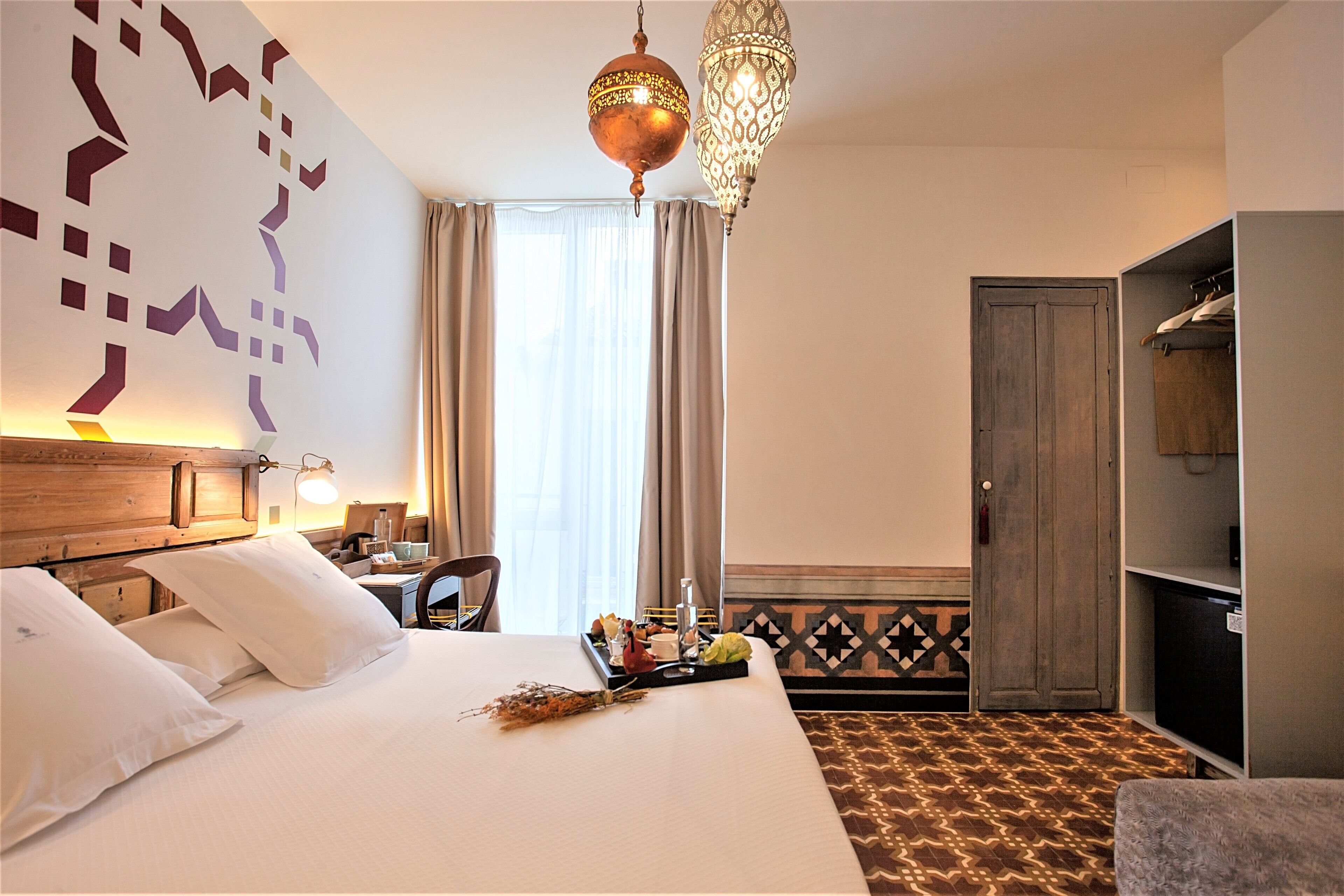 A hotel room with a large bed, a desk with a chair, a wardrobe, and a decorative wall.