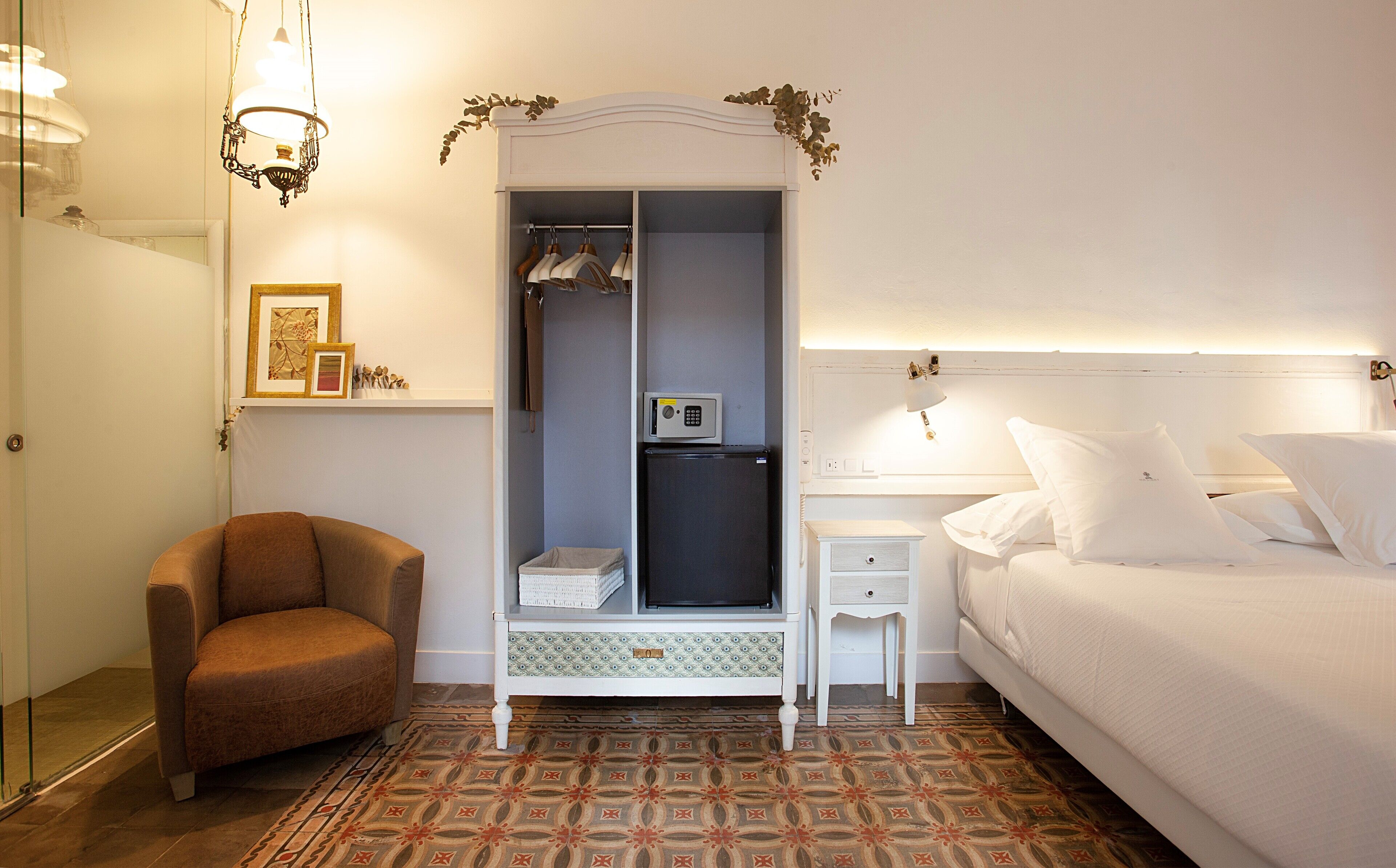 A bedroom with a bed, a wardrobe, a chair, a bedside table, and a patterned floor.