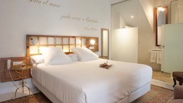 Una cama bien hecha con sábanas blancas, una mesita de noche con una lámpara y una pared con una cita decorativa.