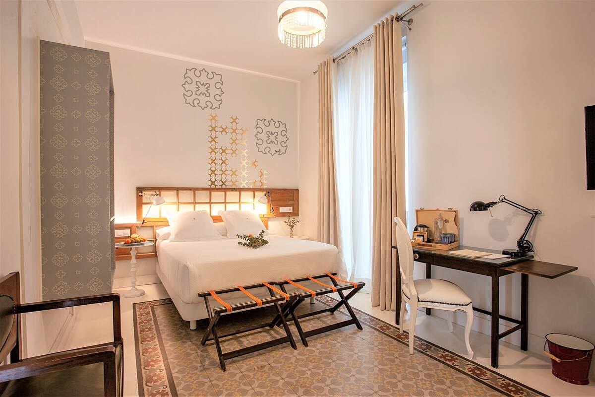 A hotel room with a bed, desk, chair, lamp, and decorative wall art.