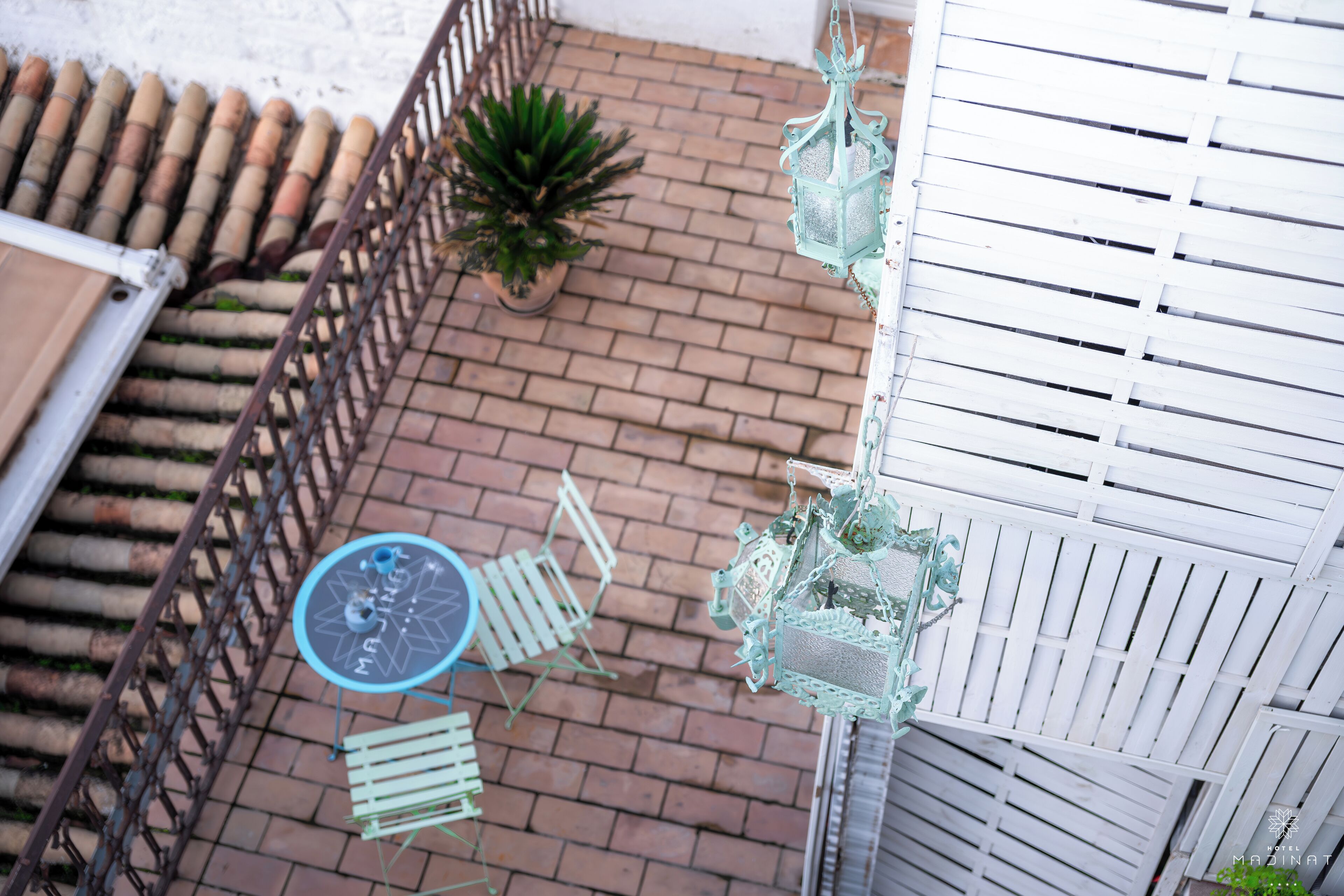 A patio with a brick floor, a potted plant, a table with chairs, and hanging lanterns.