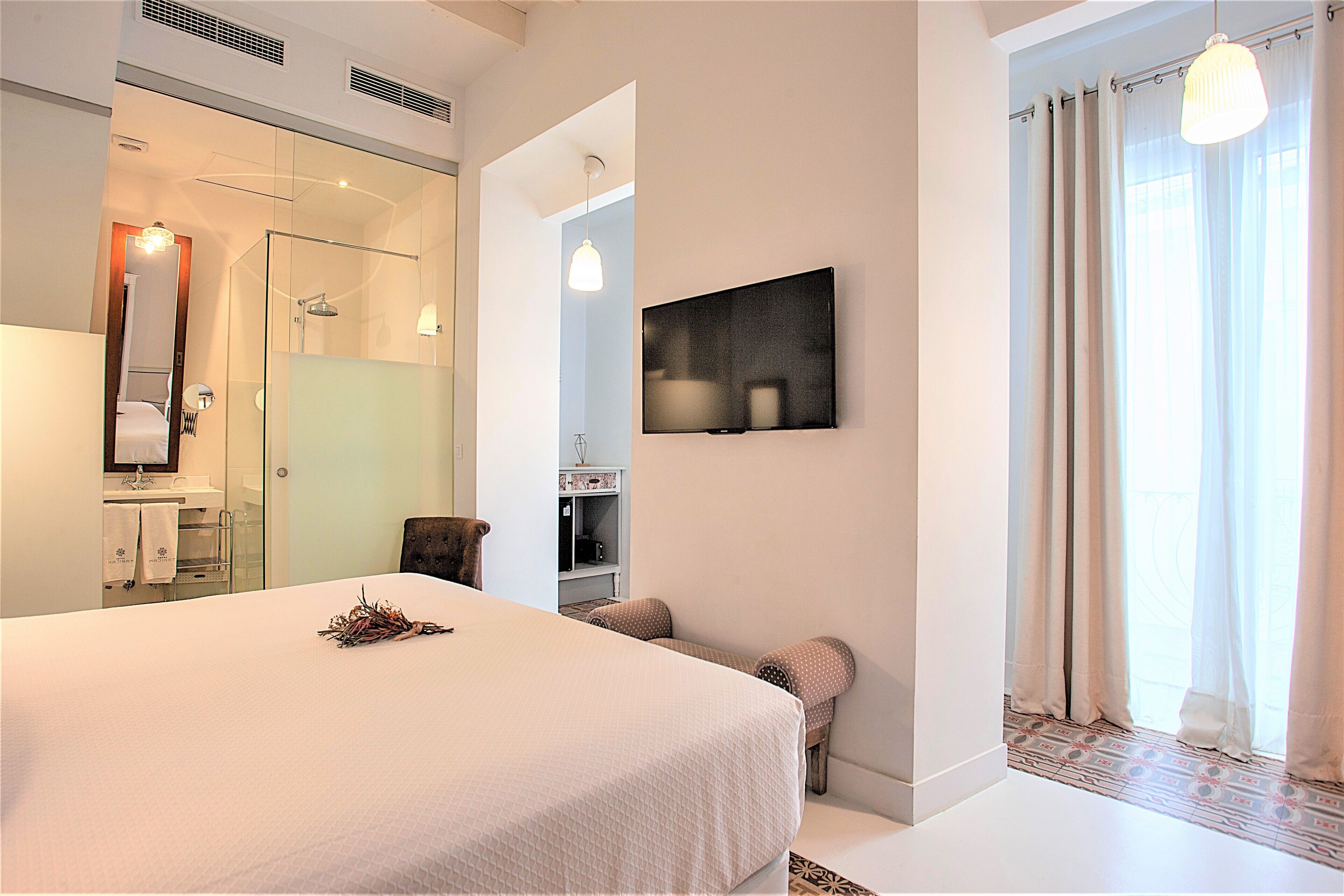 A modern hotel room with a large bed, a glass shower enclosure, a television on the wall, and a view of the outdoors through the window.