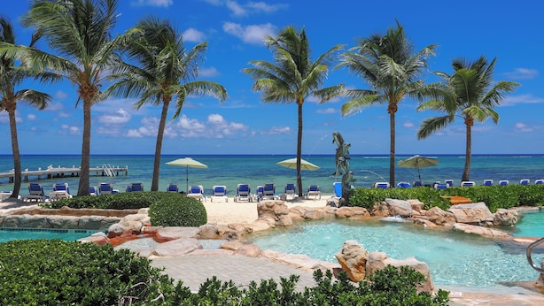 A pool area with palm trees, lounge chairs, and a view of the ocean. - The Reef Beach Resort - All Inclusive - East End, Grand Cayman (East End)