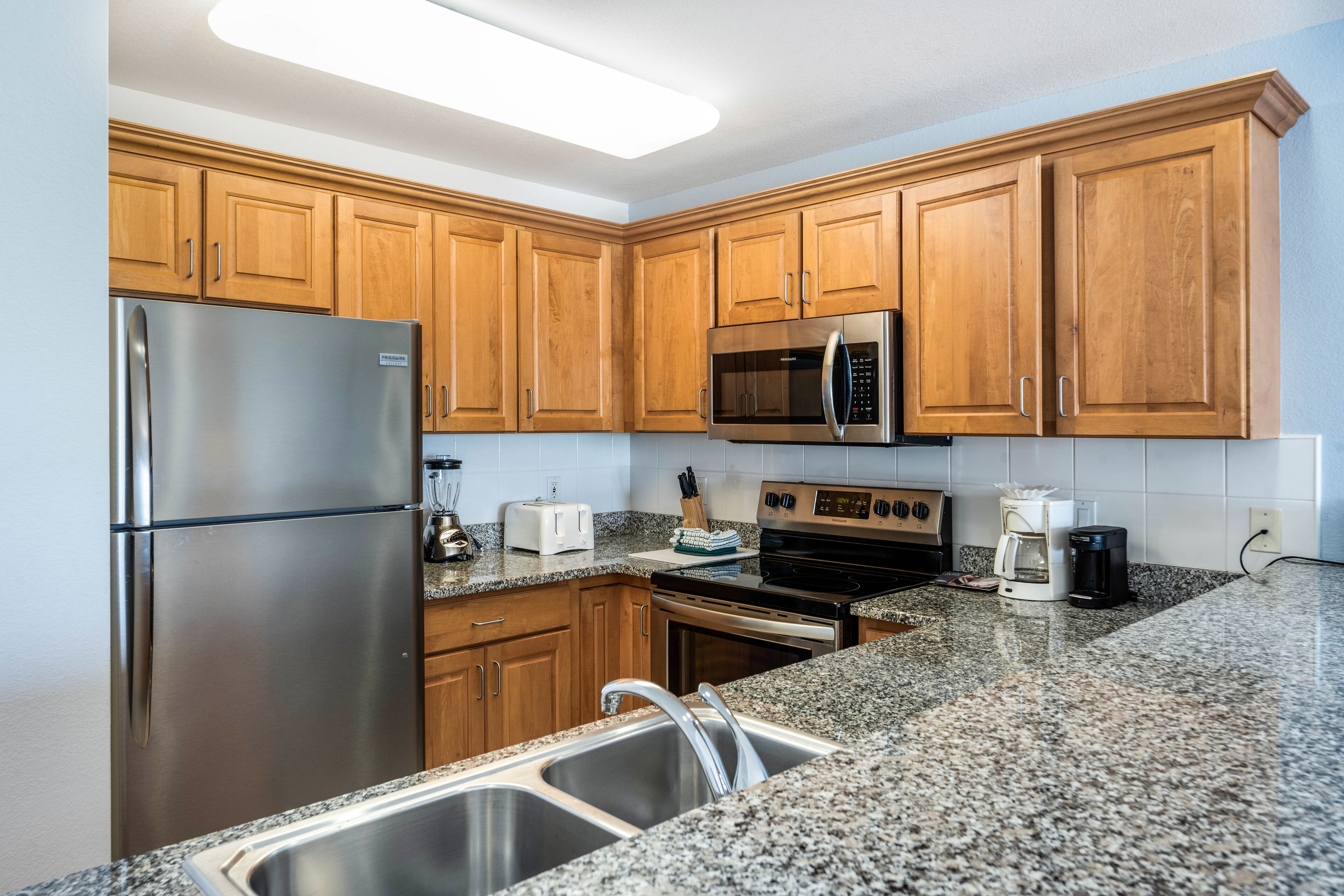 A kitchen with wooden cabinets, stainless steel appliances, granite countertops, and a double sink.