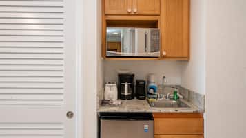 A compact kitchen with wooden cabinets, a stainless steel microwave, a coffee maker, a toaster, and a dishwasher.
