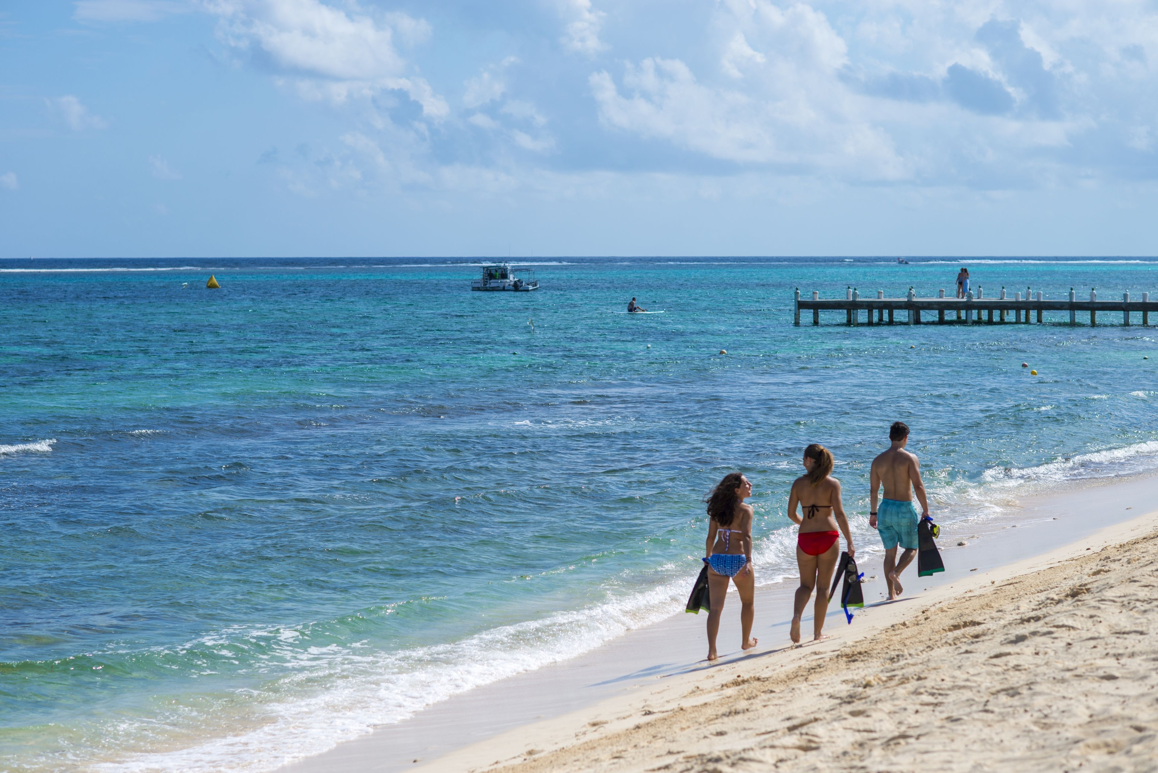 A beach with clear blue water, a pier, and a boat in the distance.