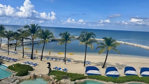 A beach with palm trees, lounge chairs, and a pool. - The Reef Beach Resort - All Inclusive - East End, Grand Cayman (East End)