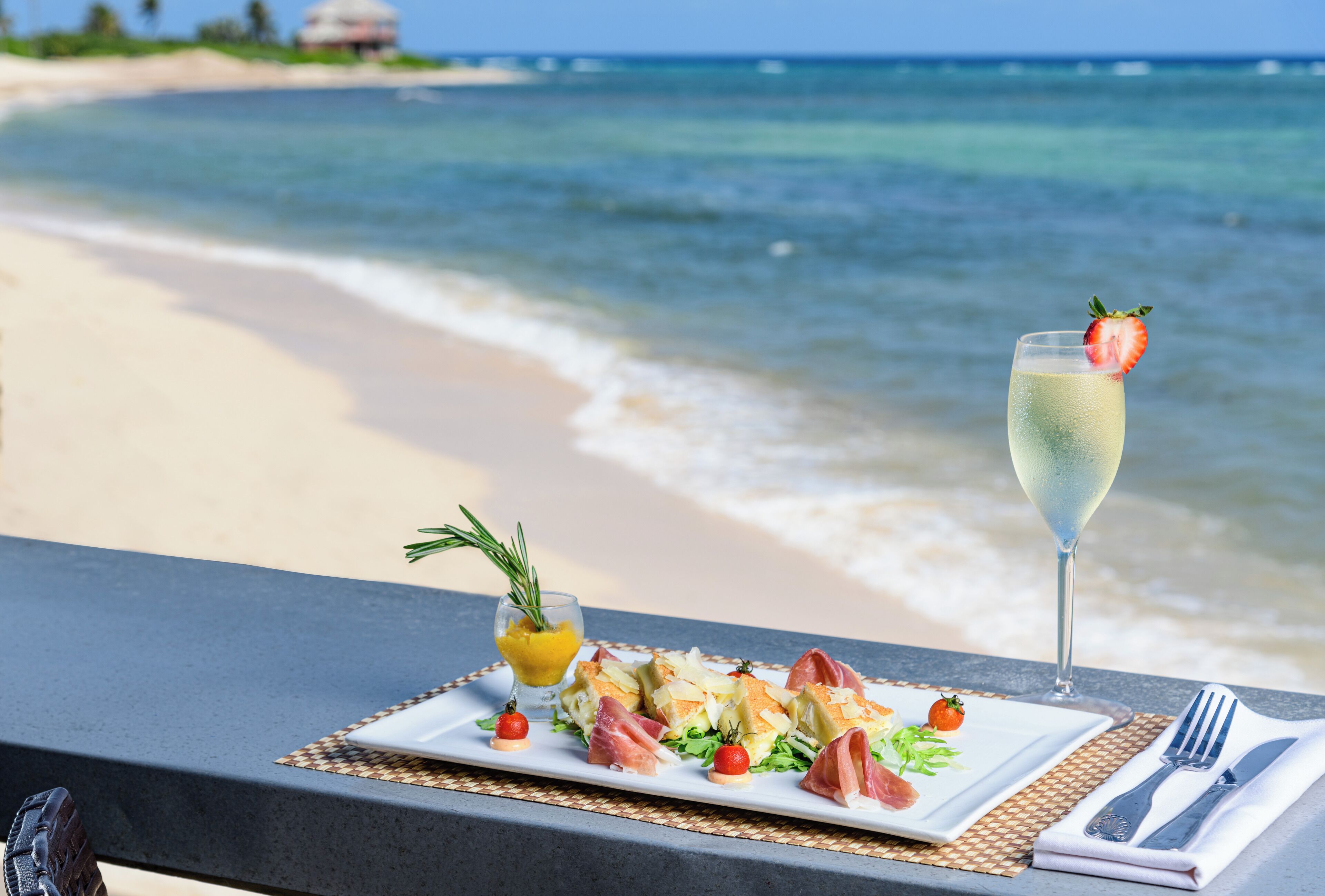 Un tavolo imbandito con un pasto e un bicchiere di champagne su un balcone con vista sulla spiaggia.