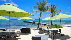 A beachside restaurant with outdoor seating, including tables and chairs, and green umbrellas providing shade. - The Reef Beach Resort - All Inclusive - East End, Grand Cayman (East End)
