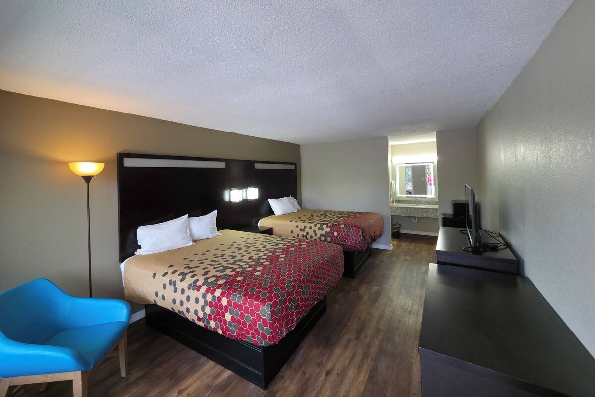 A hotel room with two beds, a desk, a chair, and a lamp.