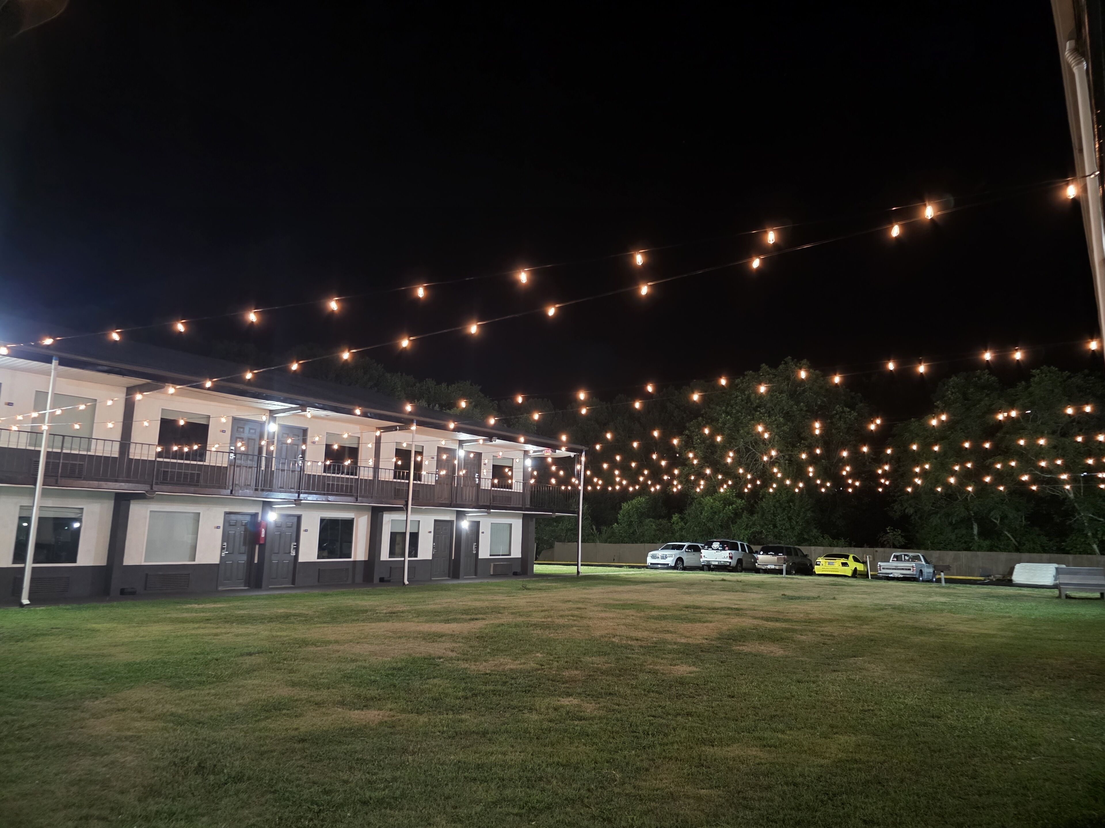 A building with multiple balconies, string lights, and parked vehicles.