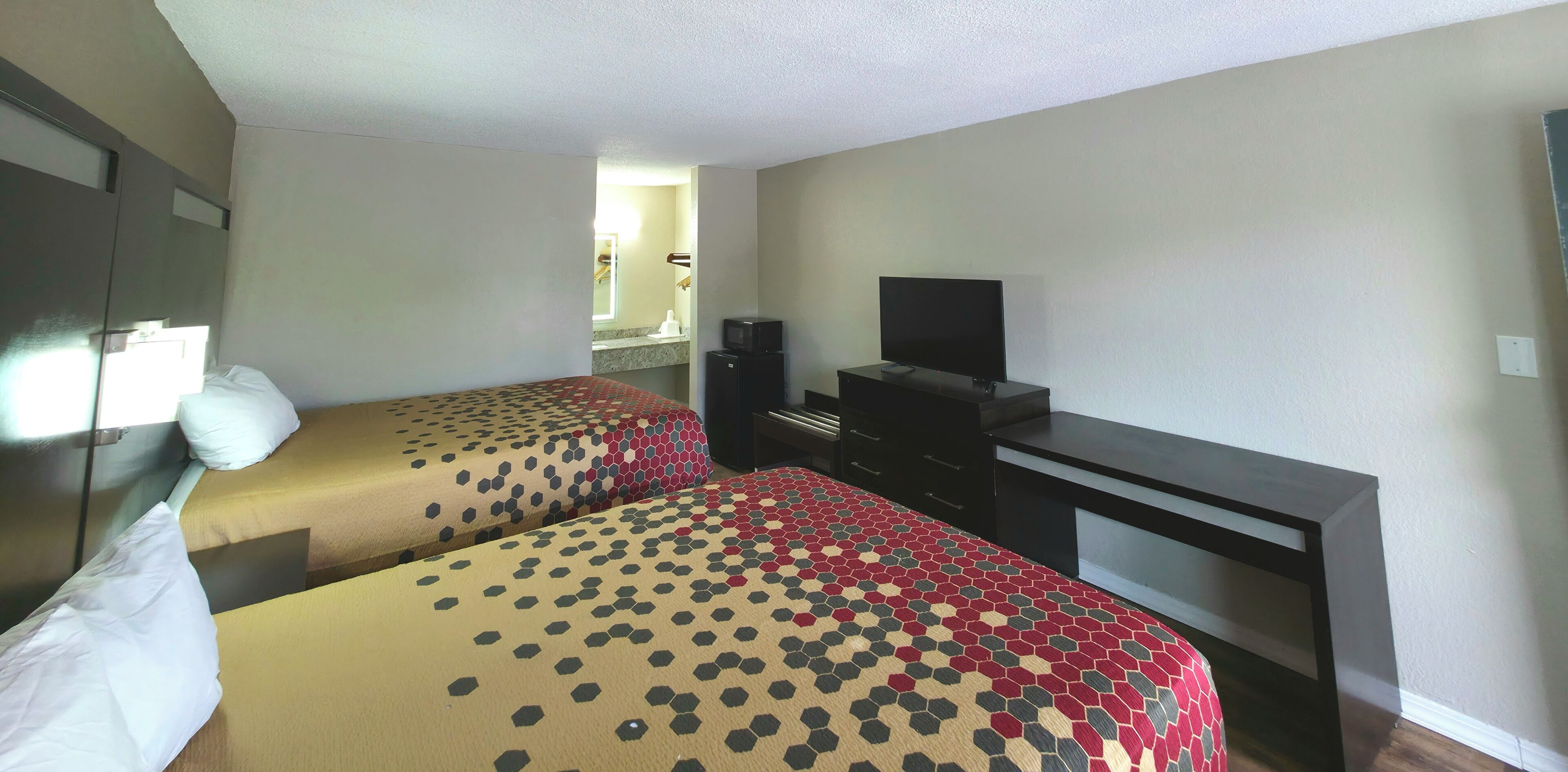 A hotel room with two beds, a TV, a desk, and a small kitchenette.