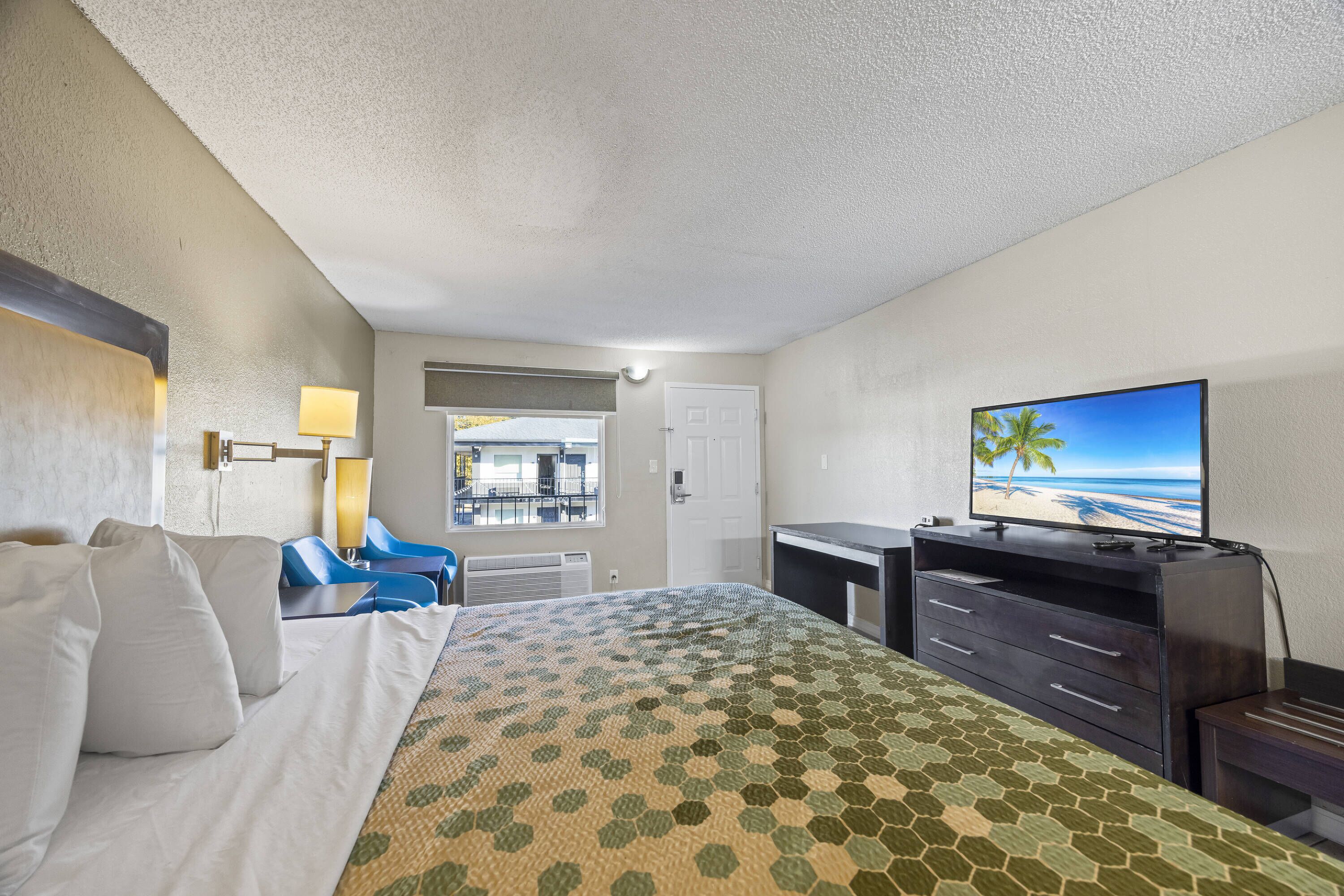 A hotel room with a bed, a desk, a television, and a view of the beach.