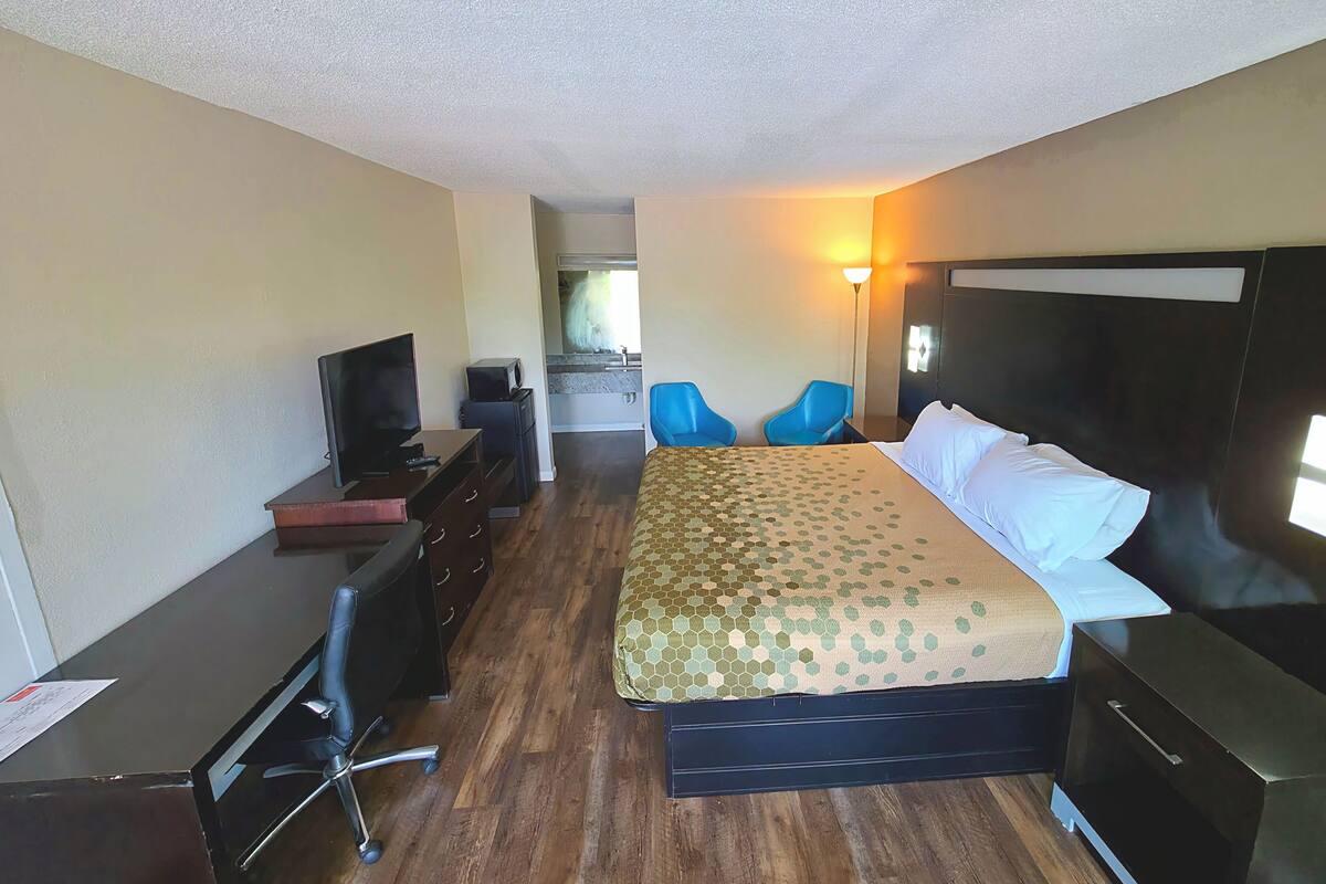 A hotel room with a bed, a desk with a chair, a television, and a bathroom visible through an open door.