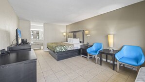 Habitación de hotel con cama, escritorio, dos sillas, televisor y baño visible a través de una puerta abierta.