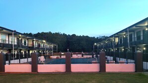 Una hilera de edificios de motel con balcones, un patio vallado y una zona de piscina.