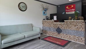 Un área de recepción con mostrador, un reloj, un sofá y una planta decorativa.