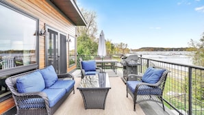 A deck with wicker furniture, a grill, and a view of a marina. - Lakeshore Vermont (Colchester)