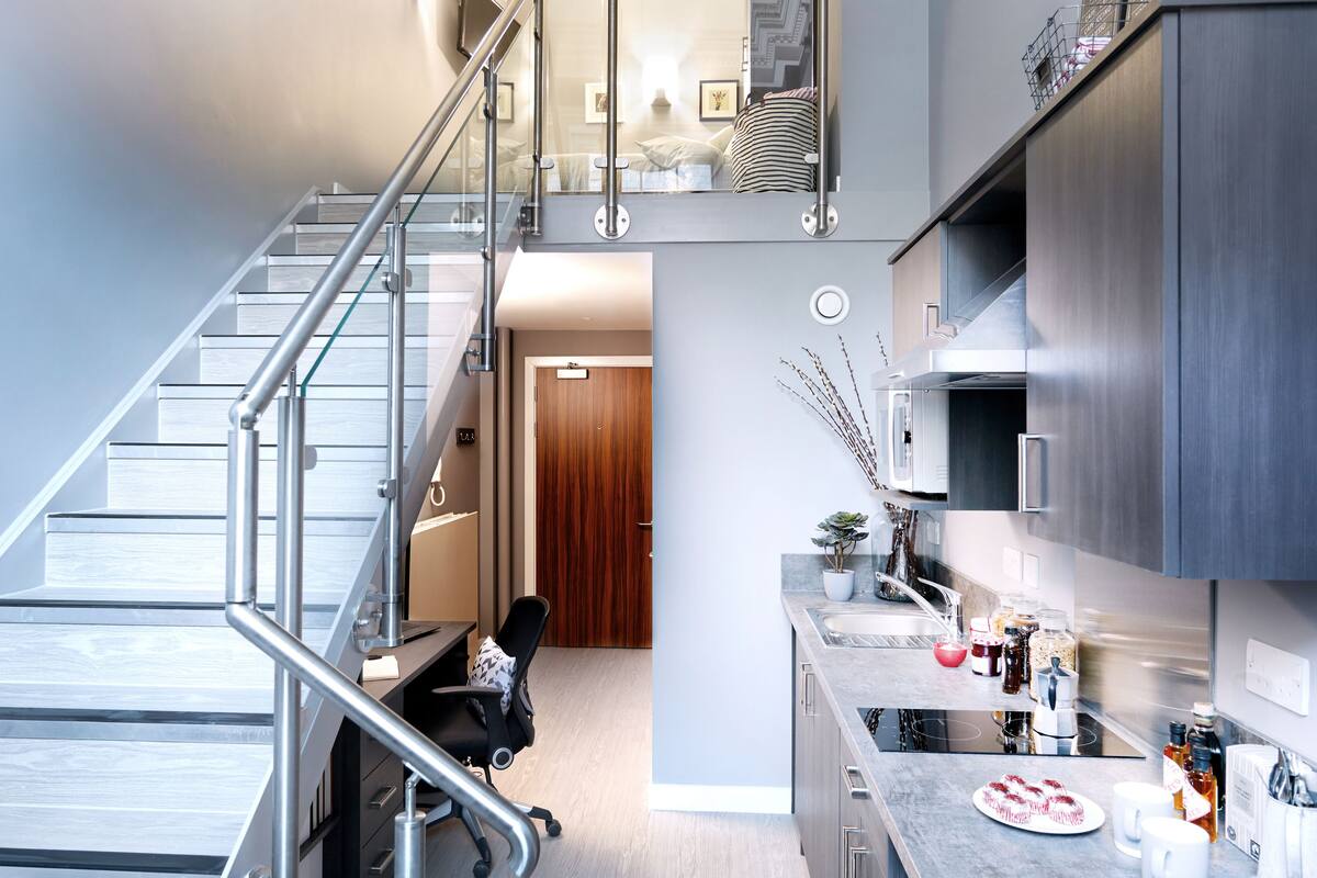 A modern kitchen with a built-in stove, a dining area with stools, and a staircase leading to an upper level.