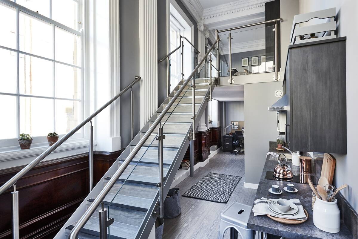 A modern kitchen with a staircase, large windows, and a dining area with bar stools.