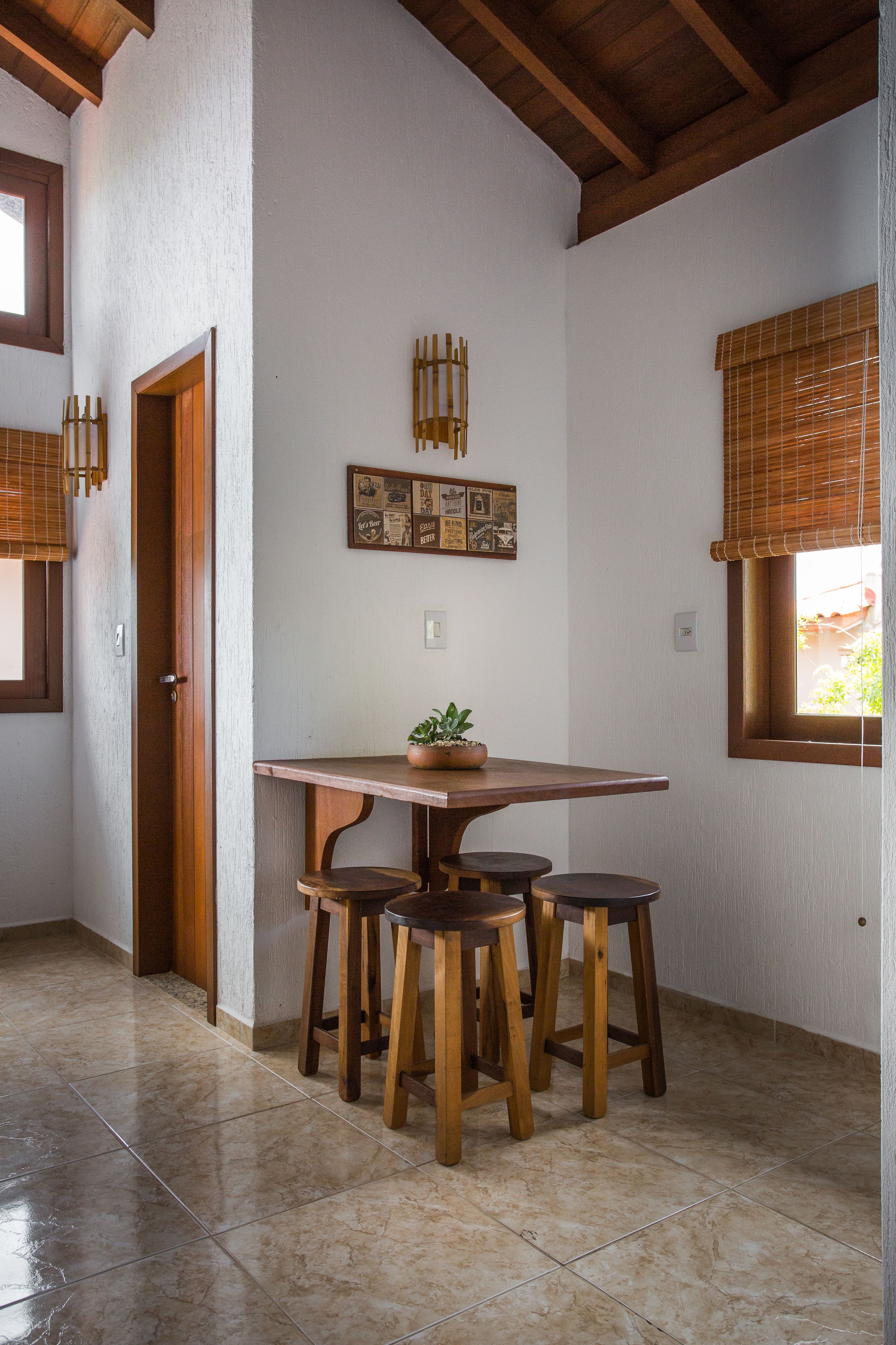 A dining area with a wooden table and stools, a potted plant, and a wall-mounted picture frame.