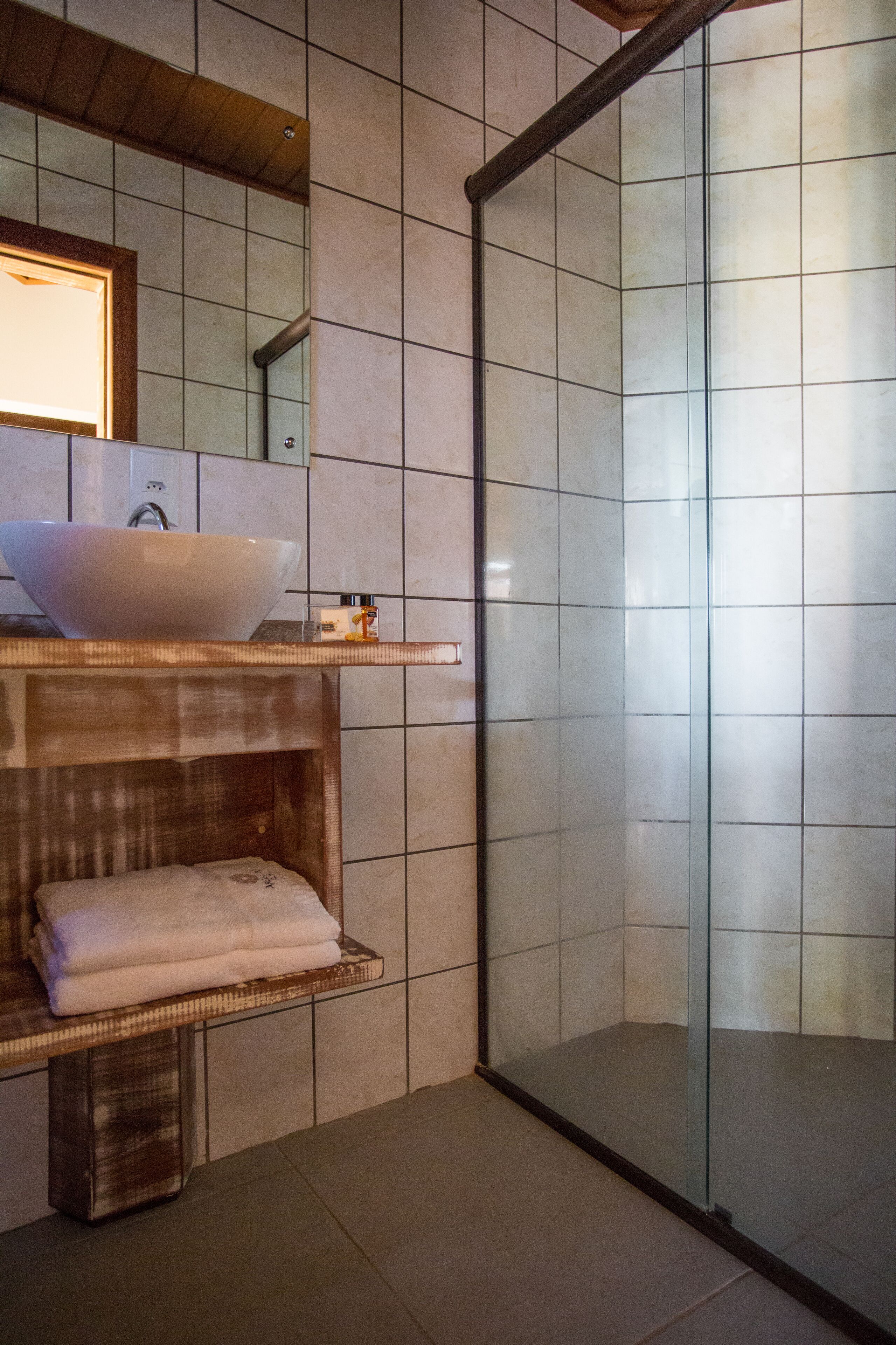 Un bagno moderno con un ampio lavabo bianco, cabina doccia in vetro e una panca in legno.