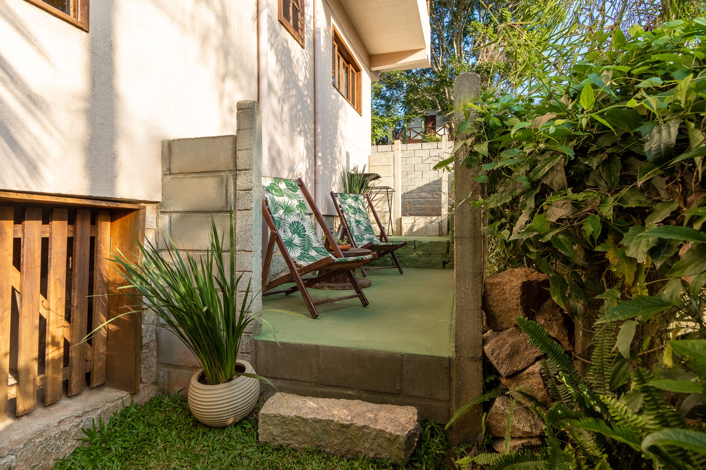 Een patio met twee houten lounge stoelen, een potplant en een stenen muur.