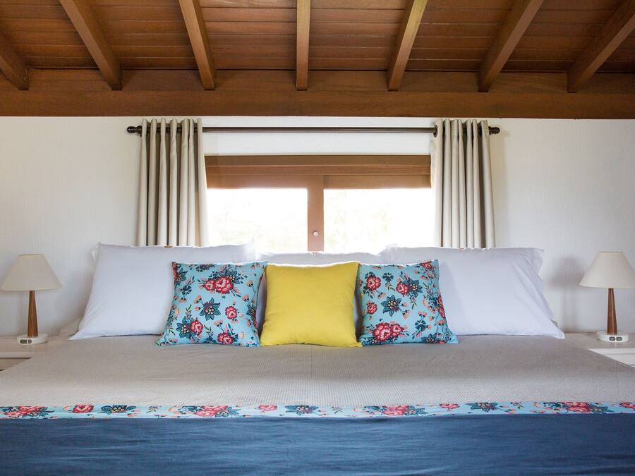 A bedroom with a bed, two nightstands, a window with curtains, and a wooden ceiling.