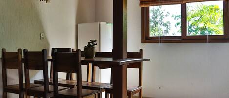 Un comedor con sillas de madera y una mesa, una ventana con vistas a la vegetación y un suelo de baldosas.