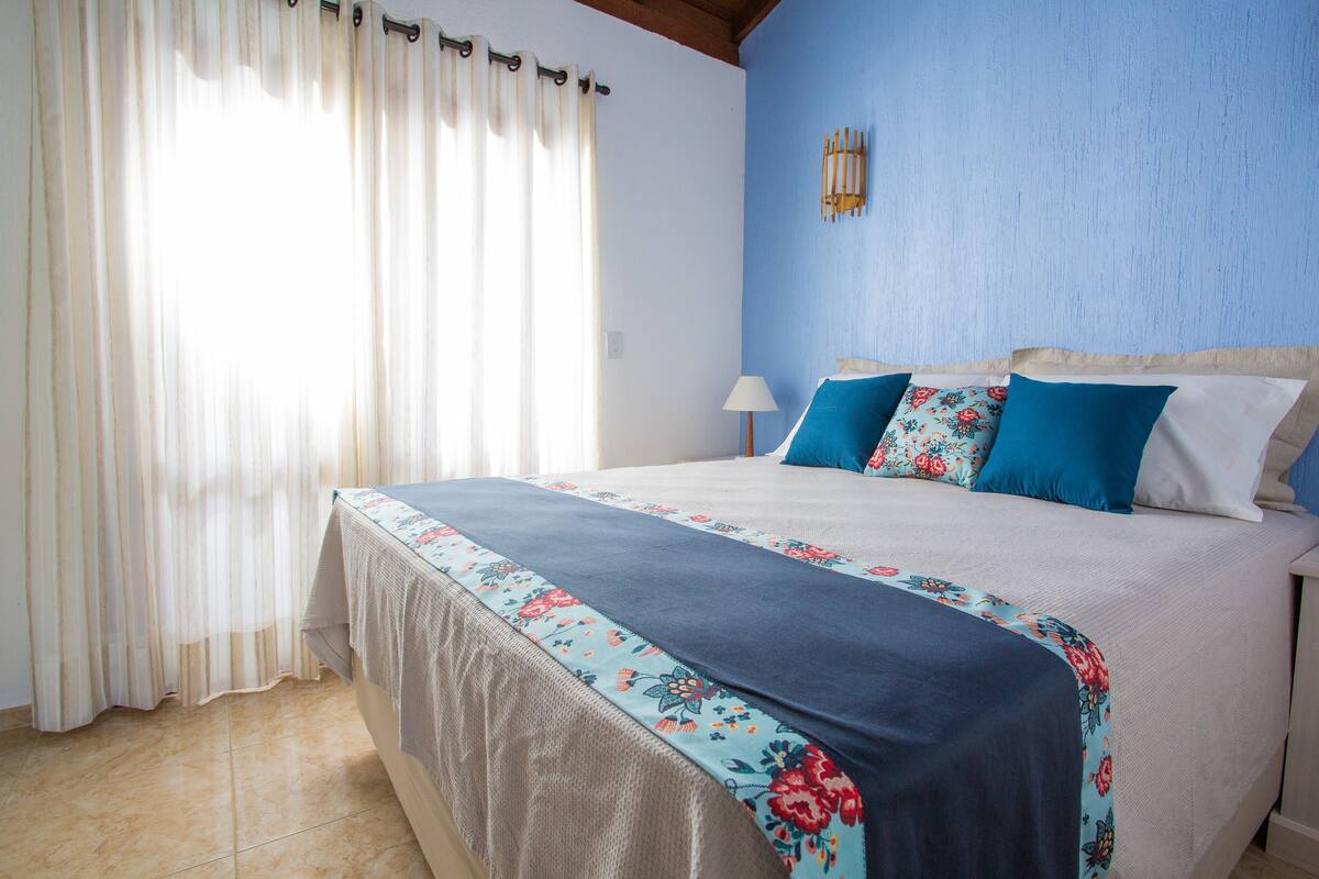 Un dormitorio con cama, cortinas, lámpara y aplique de pared.