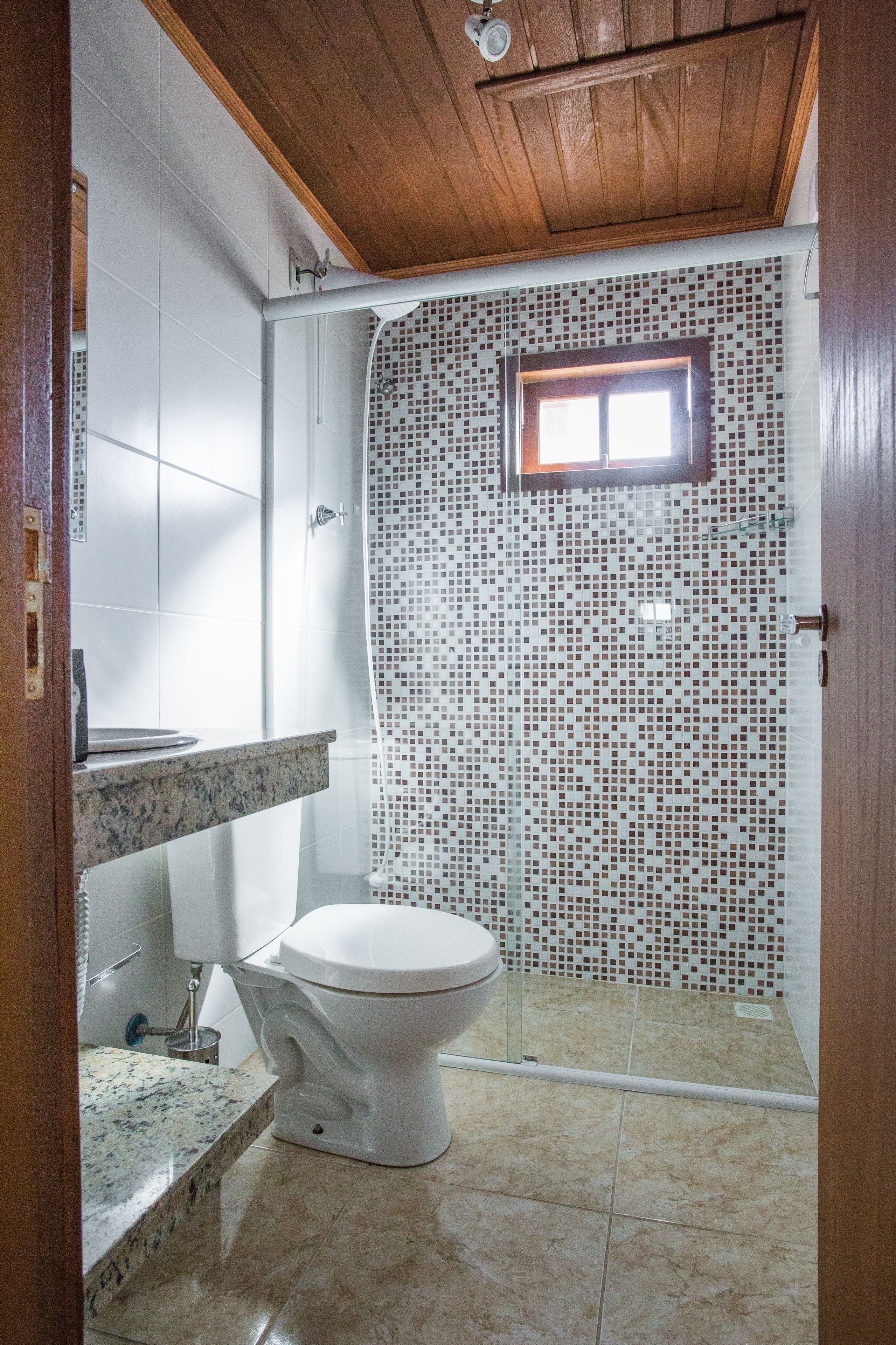A bathroom with a white toilet, a shower with mosaic tiles, and a wooden ceiling.