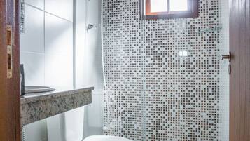 A bathroom with a white toilet, a shower with mosaic tiles, and a wooden ceiling.