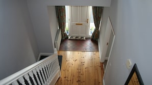 A staircase leading to a room with a wooden floor, a white door, and a view of the outside through a window with curtains.