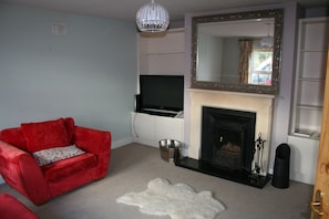 A living room with a red sofa, a flat-screen TV, a fireplace, and a mirror on the wall.