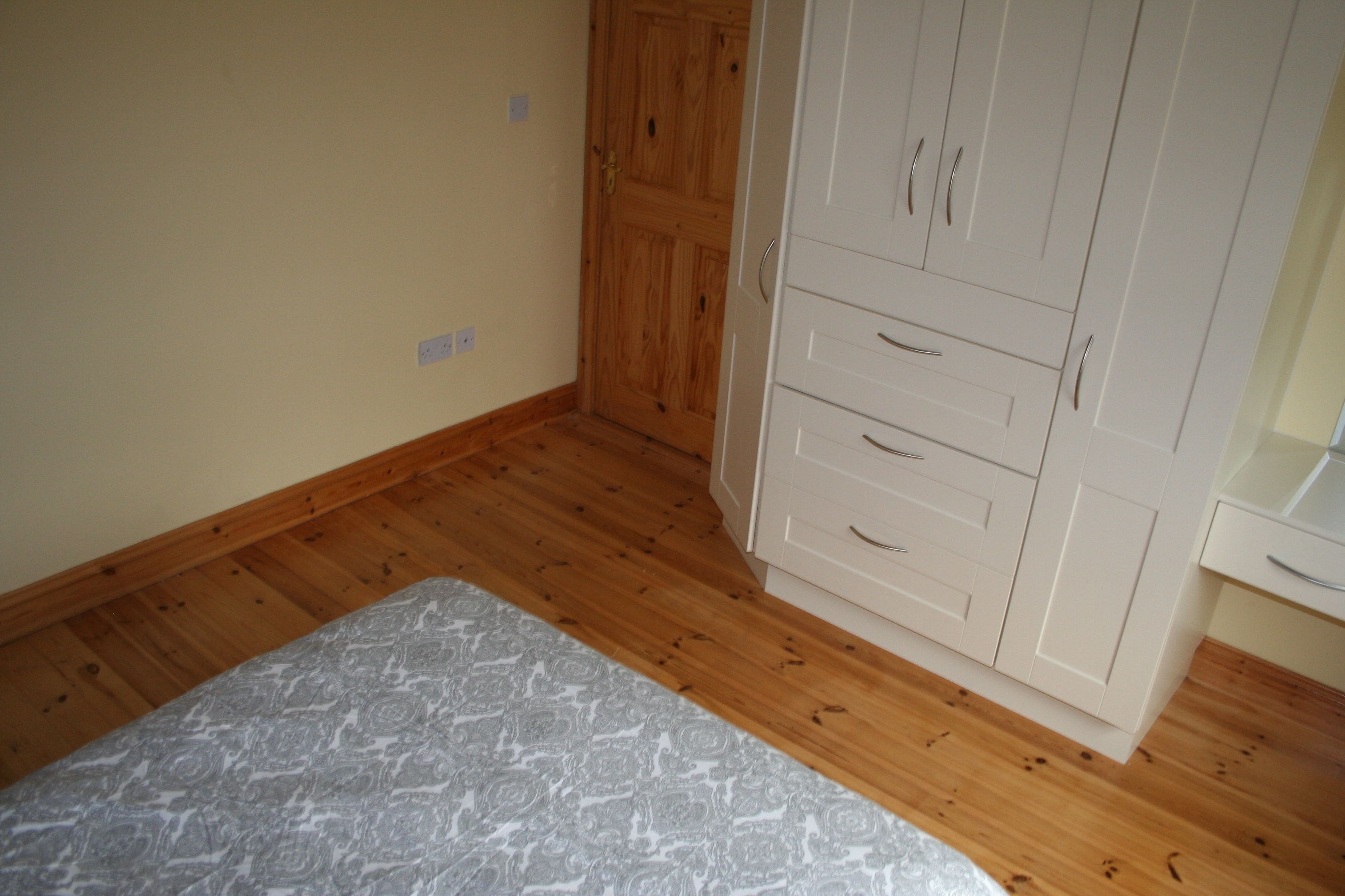 A bedroom with a bed, wooden wardrobe, and a white dresser.