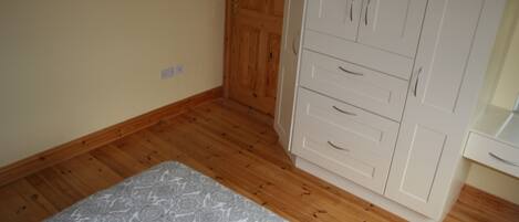 A bedroom with a bed, wooden wardrobe, and a white dresser.