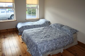 A bedroom with two beds, wooden flooring, a window with a view of a parked car, and a white wall.